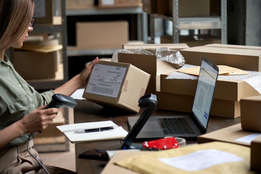 Female seller scanning ecommerce shipping box in dropshipping warehouse.